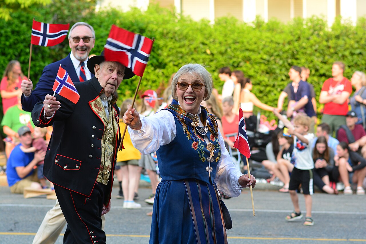 People in traditional Norwegian dress waving Norwegian flags at the Syttende Mai (Norwegian Constitution Day) parade in Seattle's Ballard neighborhood