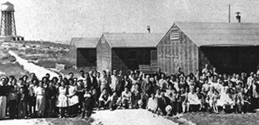 A large group of Japanese American incarcerees, including many children, standing outside wooden barracks buildings at the Minidoka incarceration camp in Idaho