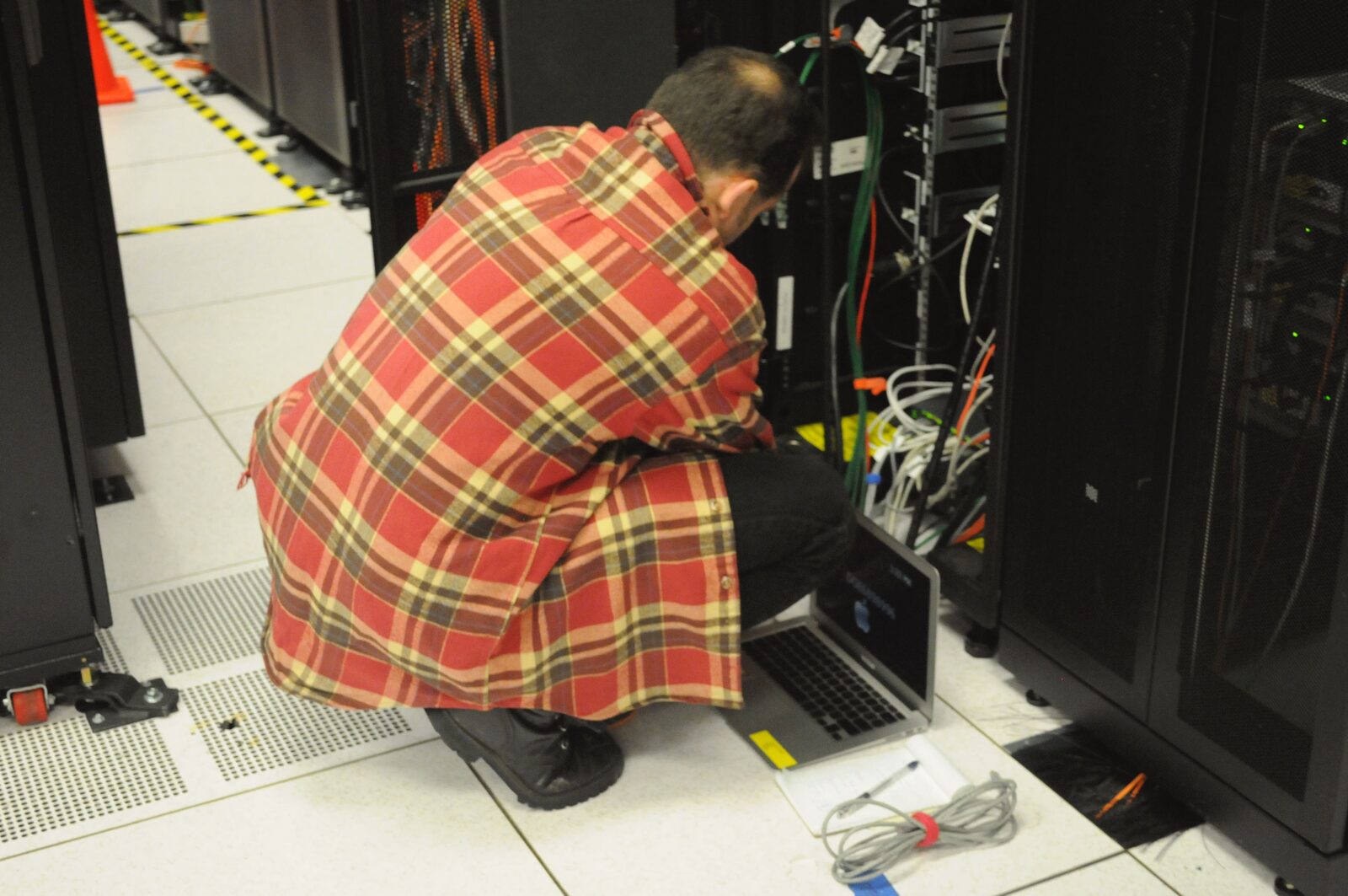 A technician crouches with a laptop, working on a server rack at a scientific computing research center